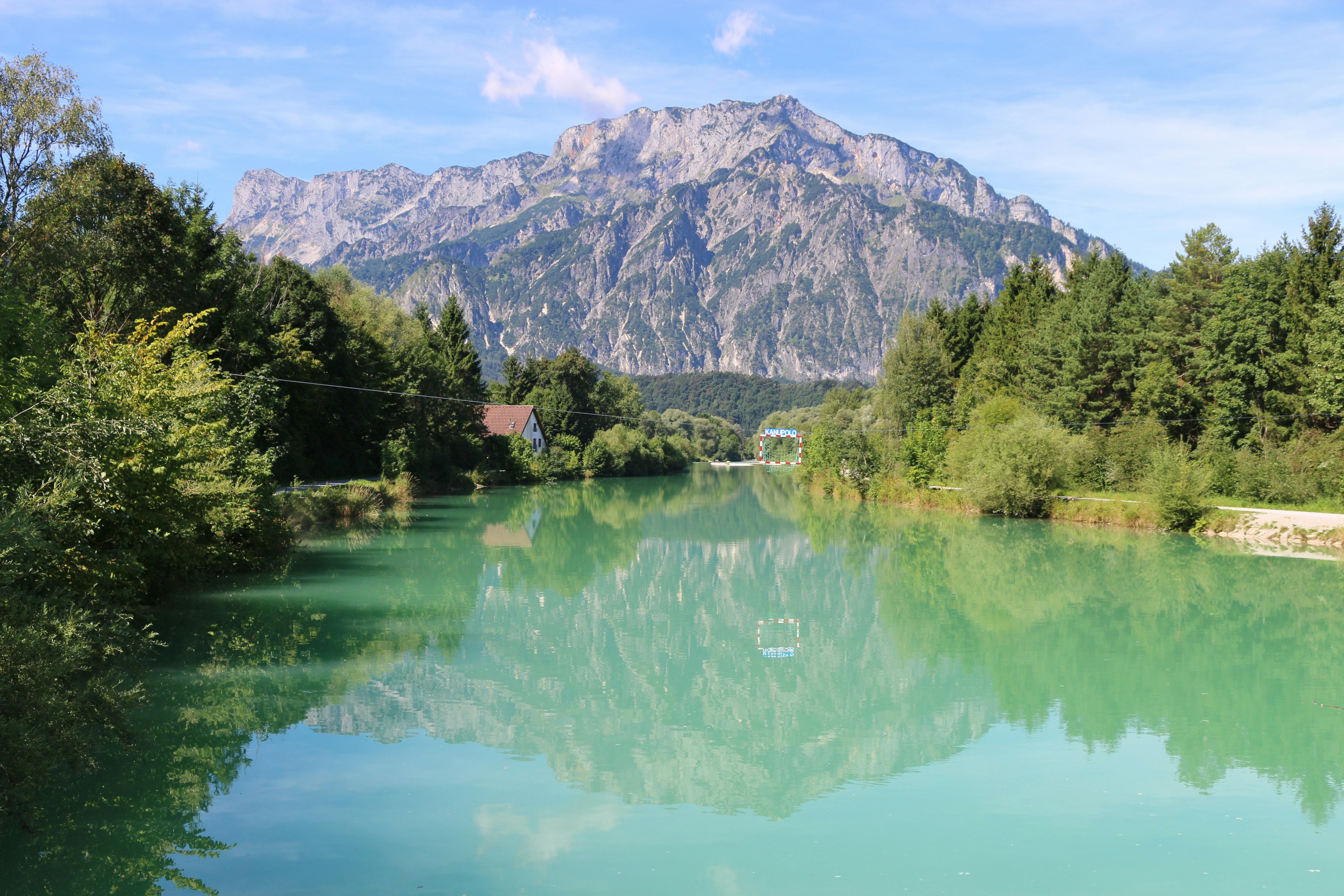 green trees near lake and mountain during daytime, Beautiful landscape with the Salzach river, in the background the mountain Untersberg. A goal for canoe polo is placed in the middle of the river. Puch, near the city Salzburg, Austria.