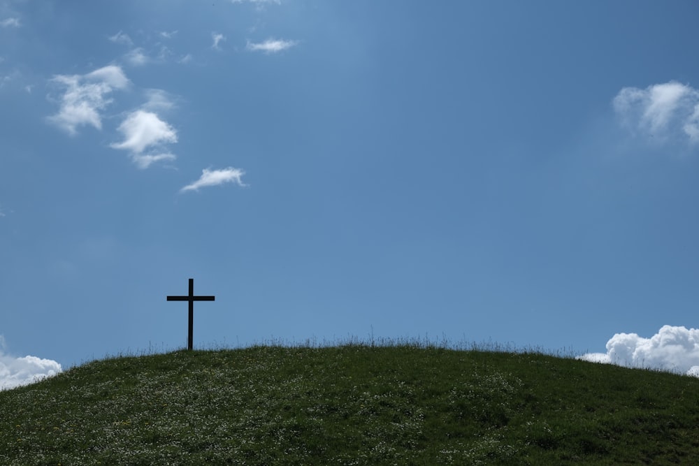 Cruz preta na grama verde sob o céu azul durante o dia