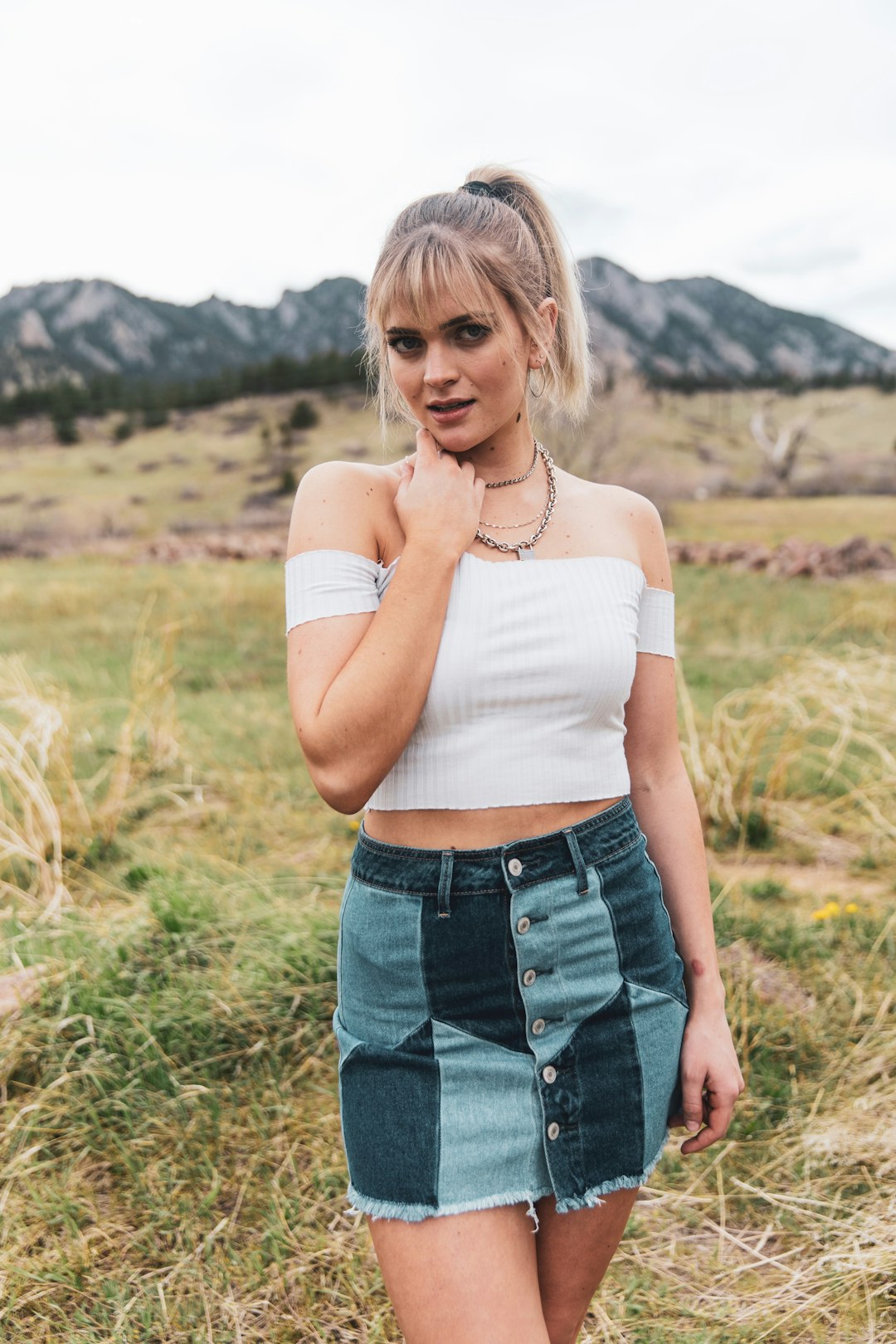 woman in white tank top and blue denim shorts standing on green grass field during daytime