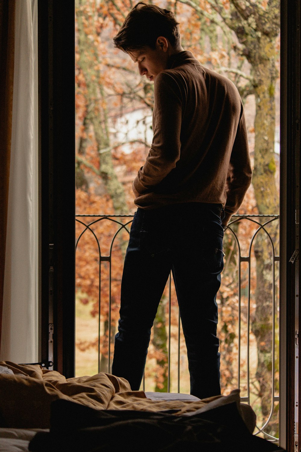 man in brown sweater and black pants standing beside glass window