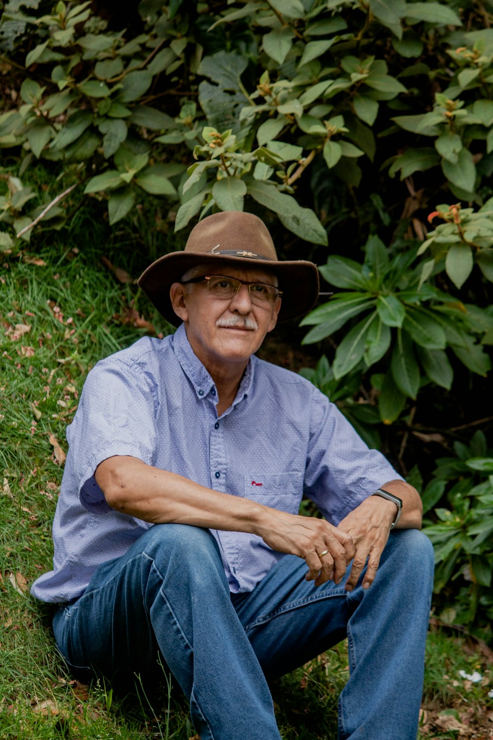 man in blue dress shirt and blue denim jeans wearing brown cowboy hat sitting on green