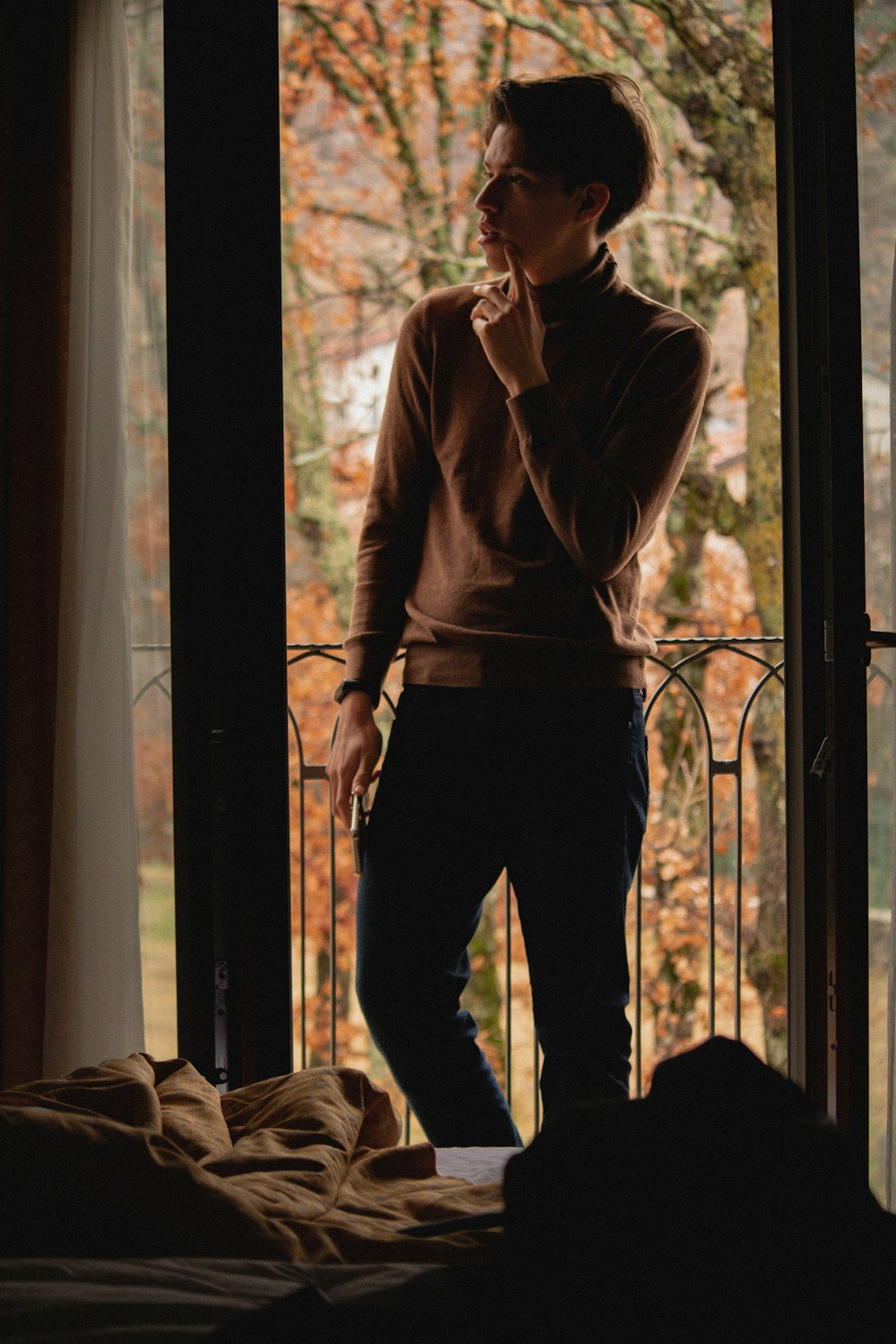 man in brown long sleeve shirt and black pants standing beside window