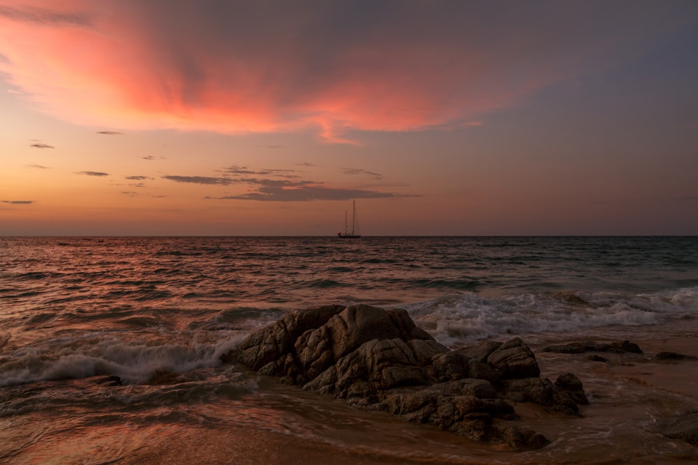 a sunset over the ocean with a sailboat in the distance