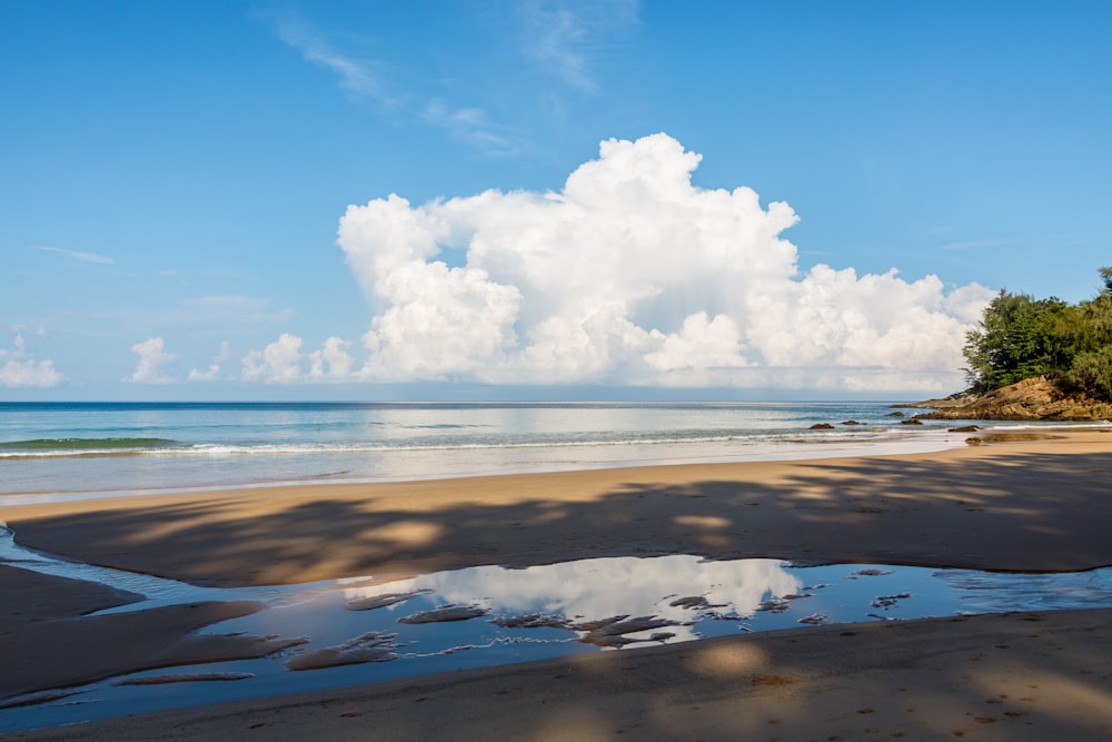 a sandy beach with water and clouds in the background