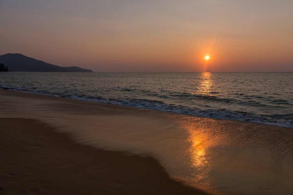 the sun is setting over the water on the beach