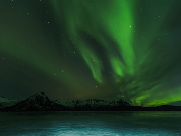 A vibrant green aurora borealis dancing over a snowy Icelandic mountain range at night.
