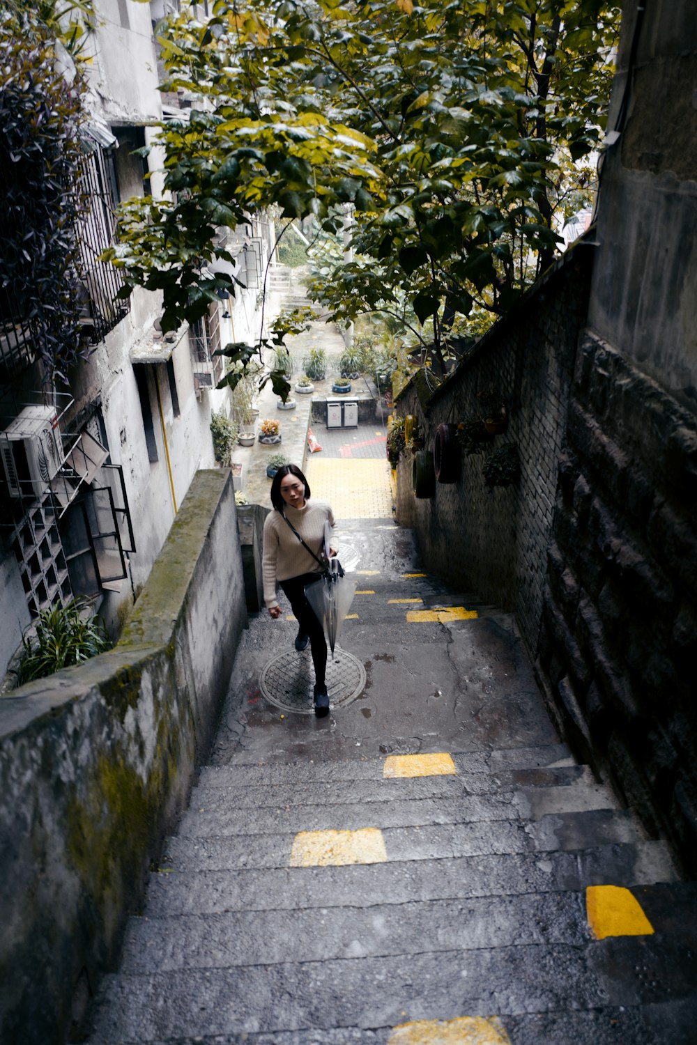Mujer con camisa blanca de manga larga y pantalones negros caminando por la acera durante el día