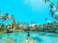 woman in black dress standing on rock near body of water during daytime