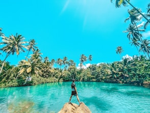 woman in black dress standing on rock near body of water during daytime