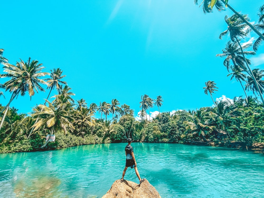 woman in black dress standing on rock near body of water during daytime