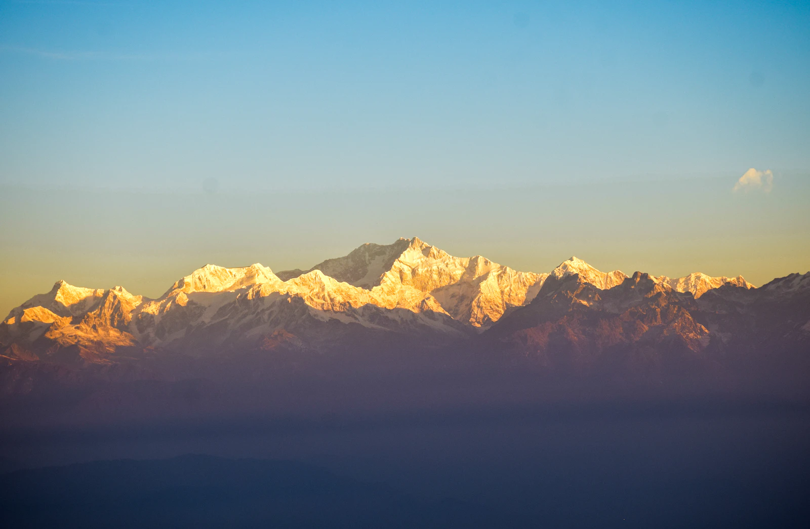 The Kanchenjunga range lit gold by the early sun above a band of haze, seen from Tiger Hill near Darjeeling