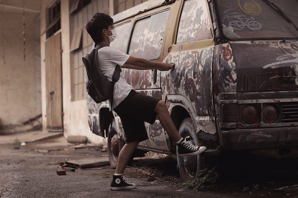 man in white shirt and black shorts sitting on brown car during daytime