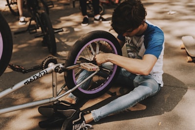 man in blue t-shirt and blue denim jeans sitting on gray concrete pavement wheel google meet background