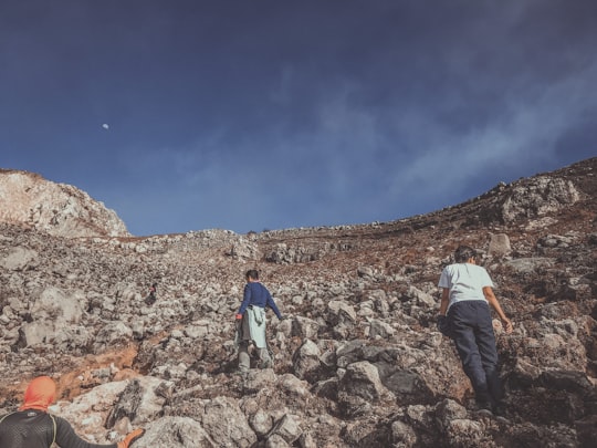 man in white jacket and blue denim jeans walking on rocky hill under blue sky during in Mount Apo Philippines