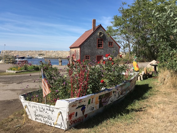 Charming seaside cottage with vibrant flowers and wooden dock extending into the sea.