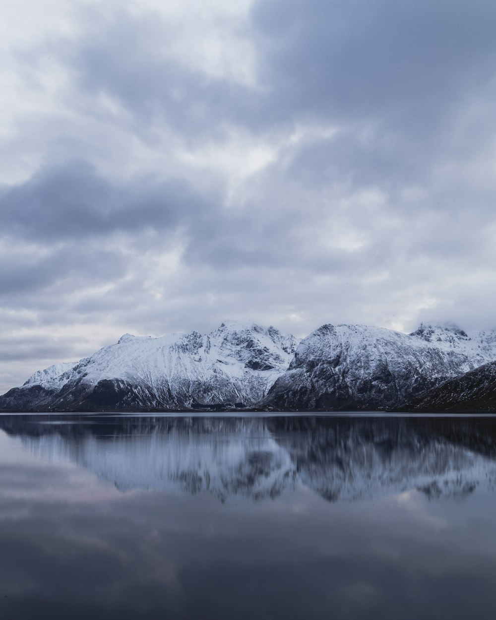 snow covered mountain near lake under cloudy sky during daytime