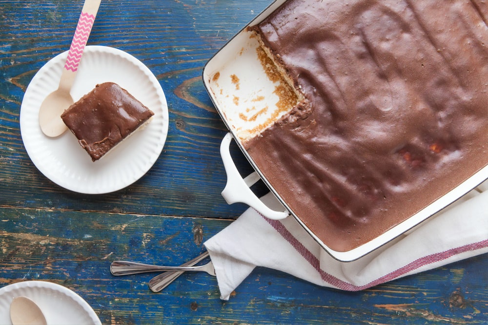 gâteau au chocolat sur assiette jetable blanche à côté d’une fourchette et d’un couteau à pain