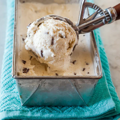A scoop being lifted from an ice cream tub in the case