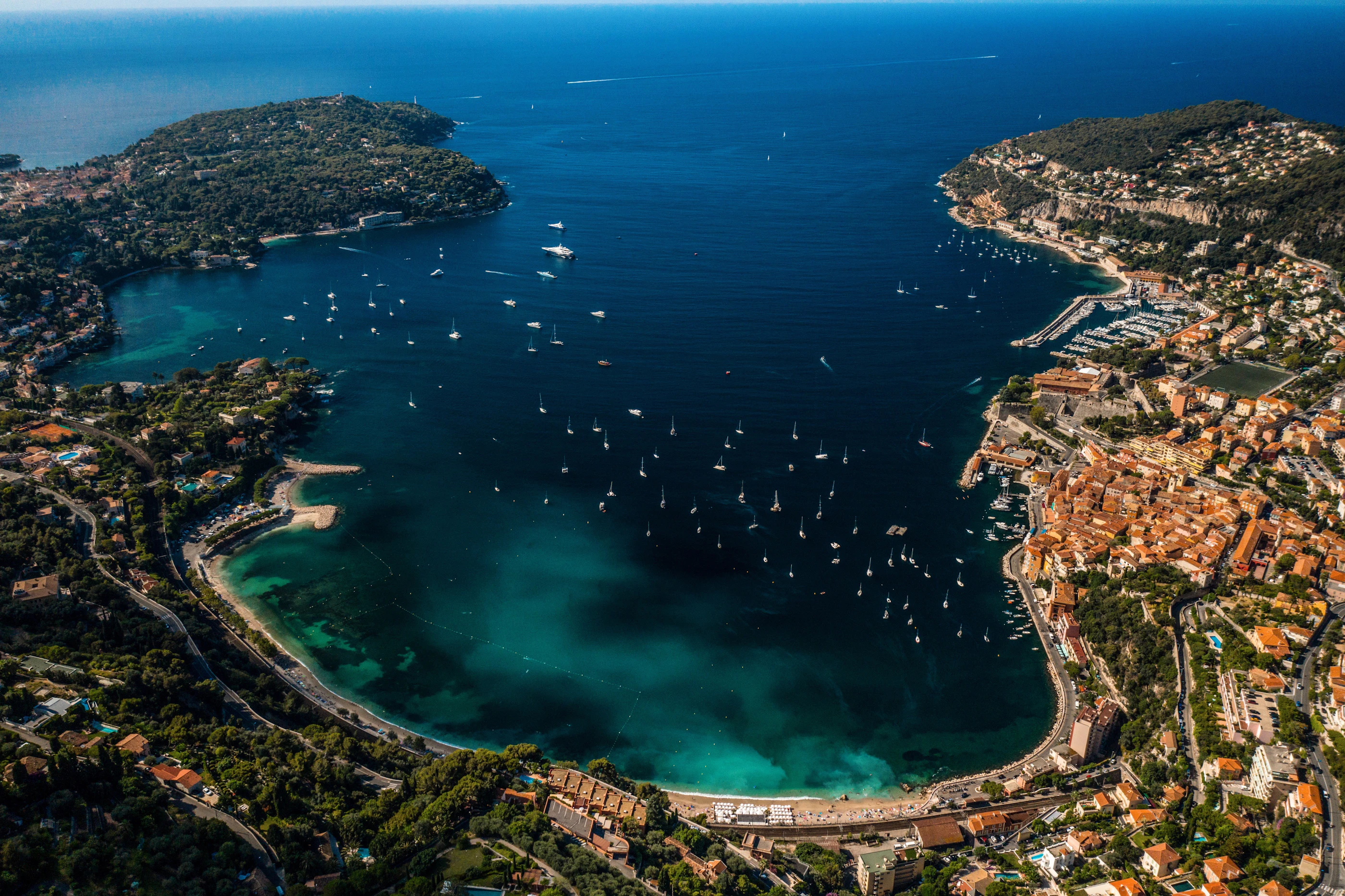 The bay of Villefranche-sur-Mer from the air, yachts at anchor in deep blue water between Cap Ferrat and the old town