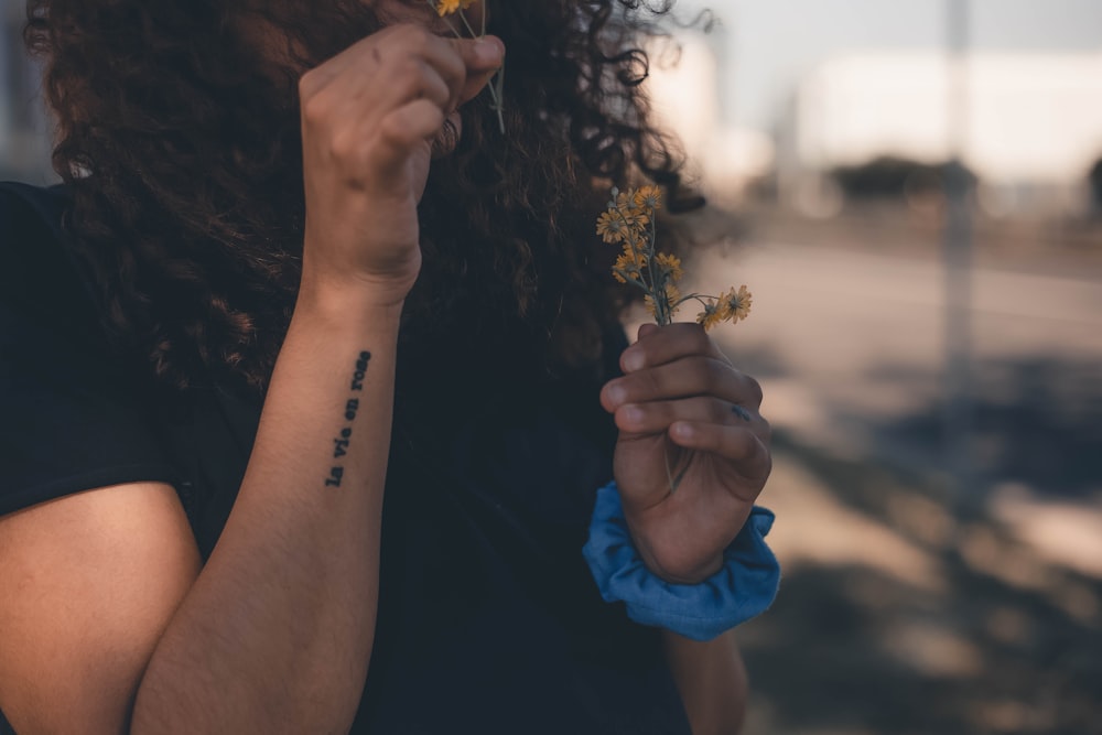 woman in black shirt holding yellow flower