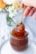 A spoon dipping into golden peach jelly with fresh peaches in the background.
