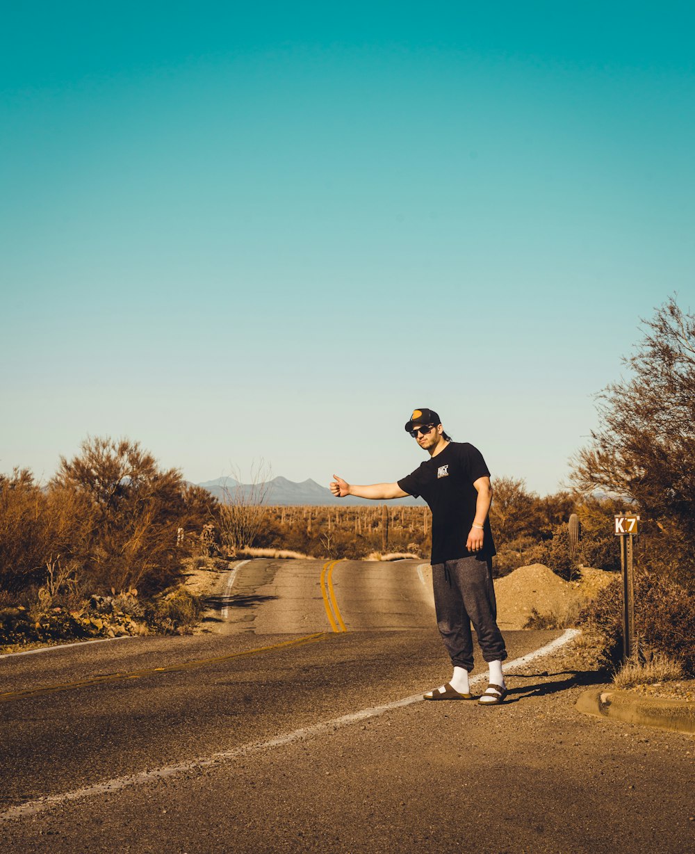 man in black shirt and blue denim jeans standing on road during daytime