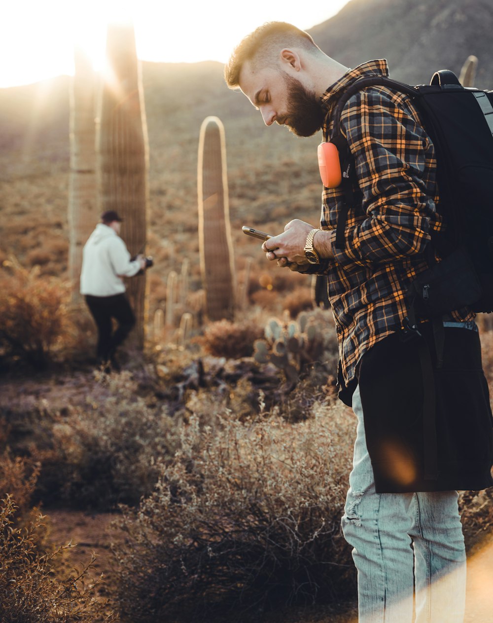 man in black and white plaid dress shirt and blue denim jeans holding white smartphone during