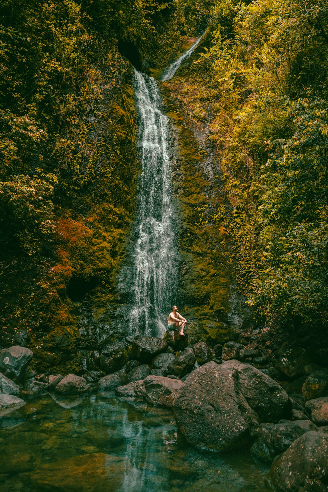 woman in white shirt sitting on rock near waterfalls during daytime