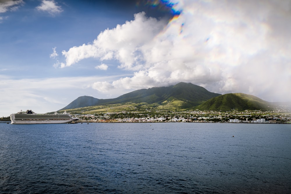 green mountain beside body of water under white clouds and blue sky during daytime