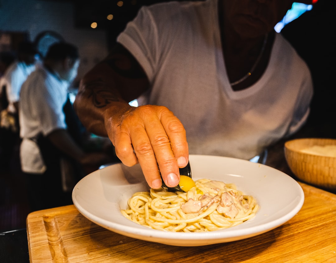person in gray long sleeve shirt holding white ceramic plate with pasta