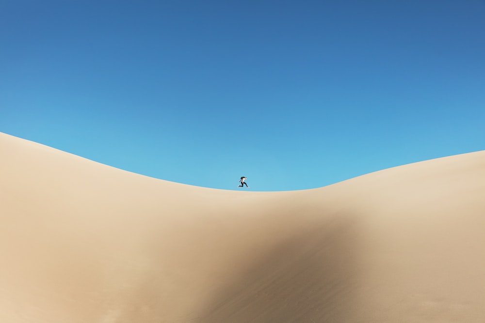 昼間、青空の下、砂漠を歩く人