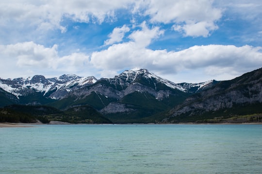 body of water near mountain under white clouds and blue sky during daytime in Barrier Lake Canada
