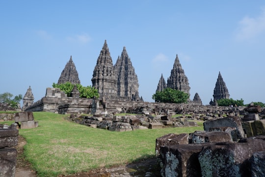 gray concrete ruins on green grass field under blue sky during daytime in Prambanan Temple Indonesia