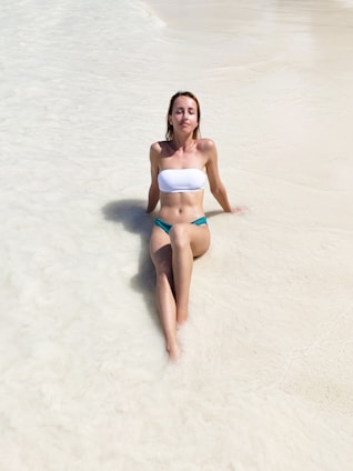 woman in blue and white bikini sitting on white sand during daytime