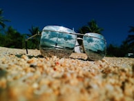 A flat lay of sunglasses and summer accessories on a sandy beach.
