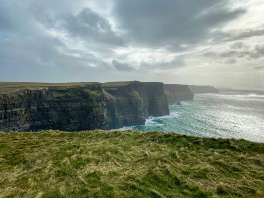 Green grass field near body of water under cloudy sky during daytime — Cliffs of Moher & the Burren, Ireland