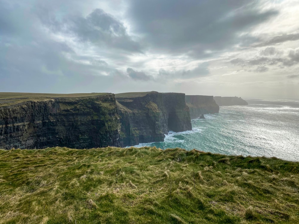 Champ d’herbe verte près d’un plan d’eau sous un ciel nuageux pendant la journée