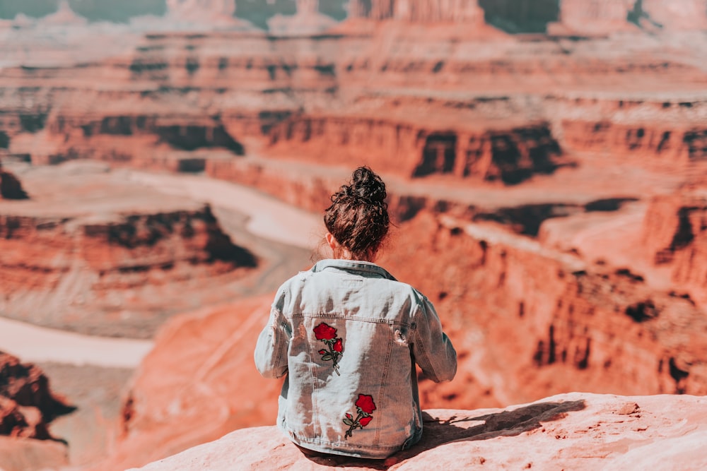 woman in white and red floral shirt sitting on rock formation during daytime