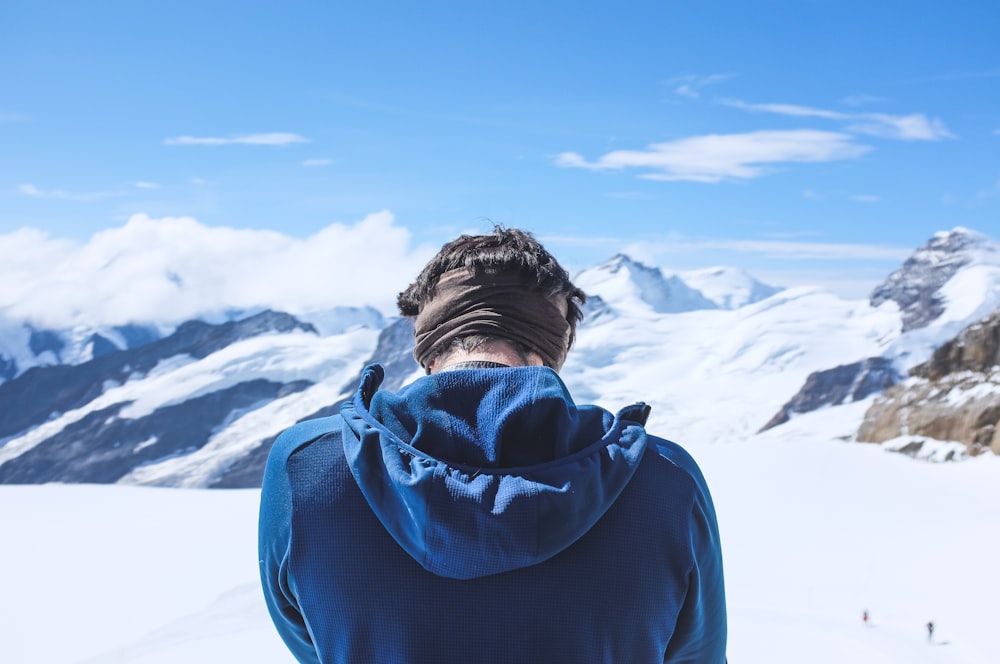 man in blue hoodie standing on snow covered ground during daytime