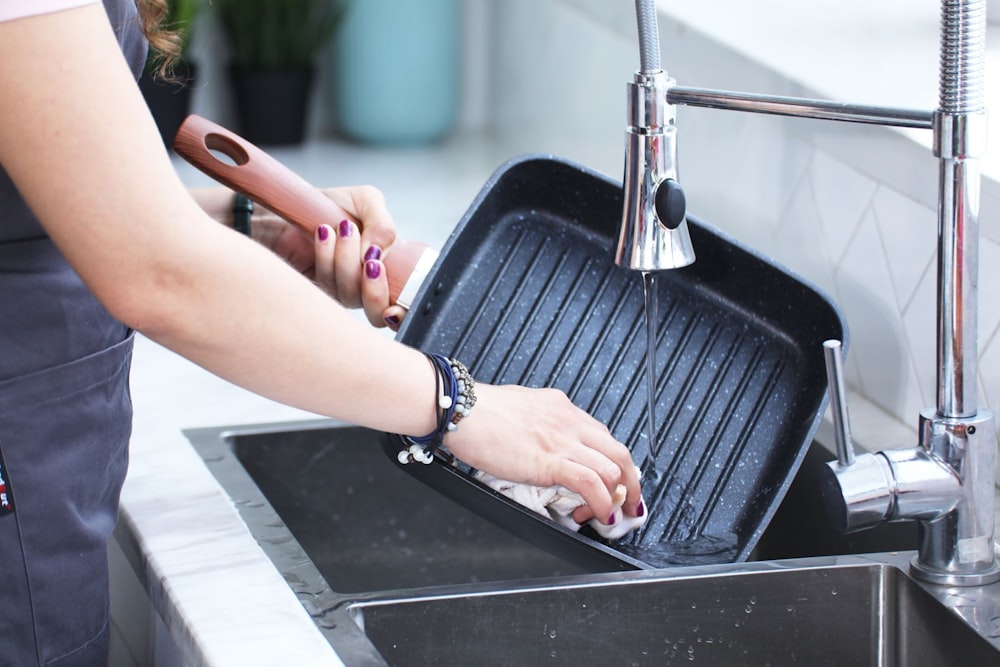 a woman washing a grill in a kitchen sink