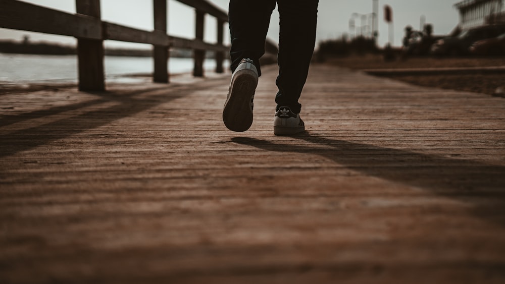 person in black pants and black shoes standing on brown wooden dock during daytime