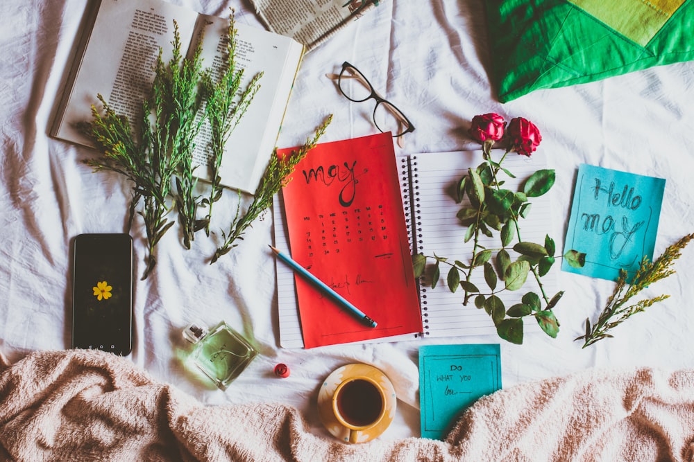 red notebook beside white ceramic mug on white textile