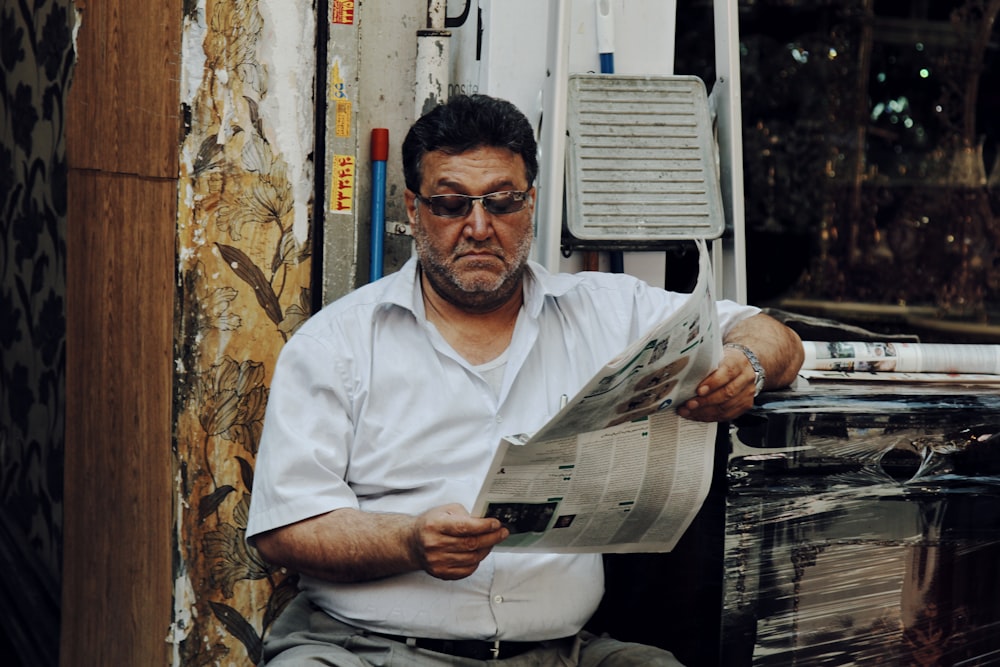 hombre en polo blanco leyendo periódico