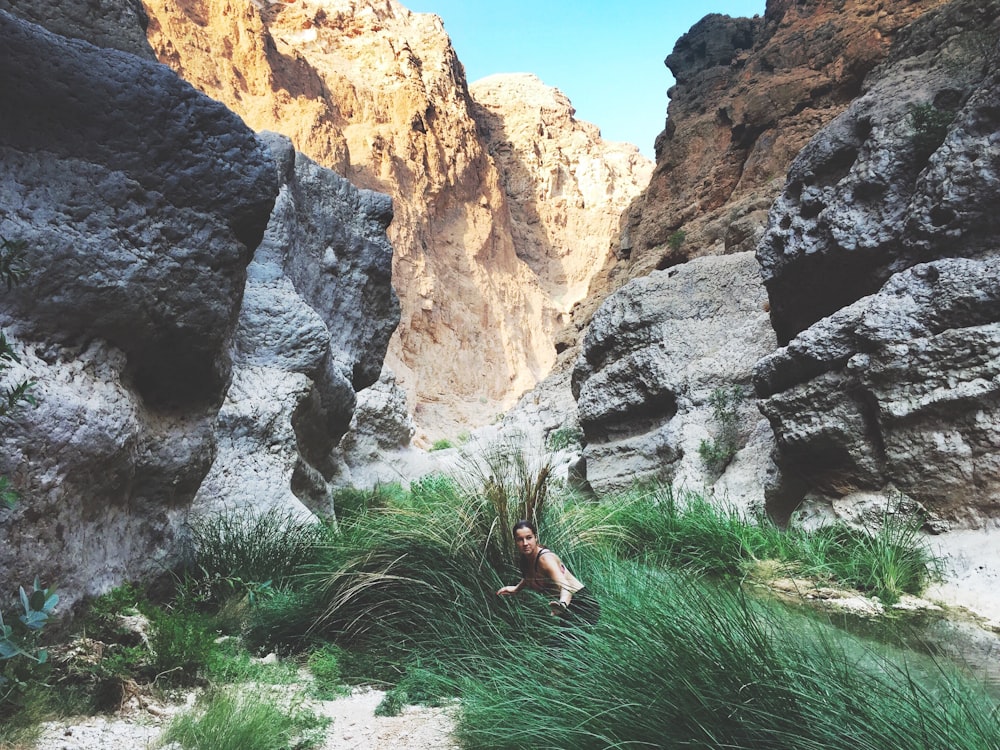 woman in black dress standing on green grass near brown rock formation during daytime