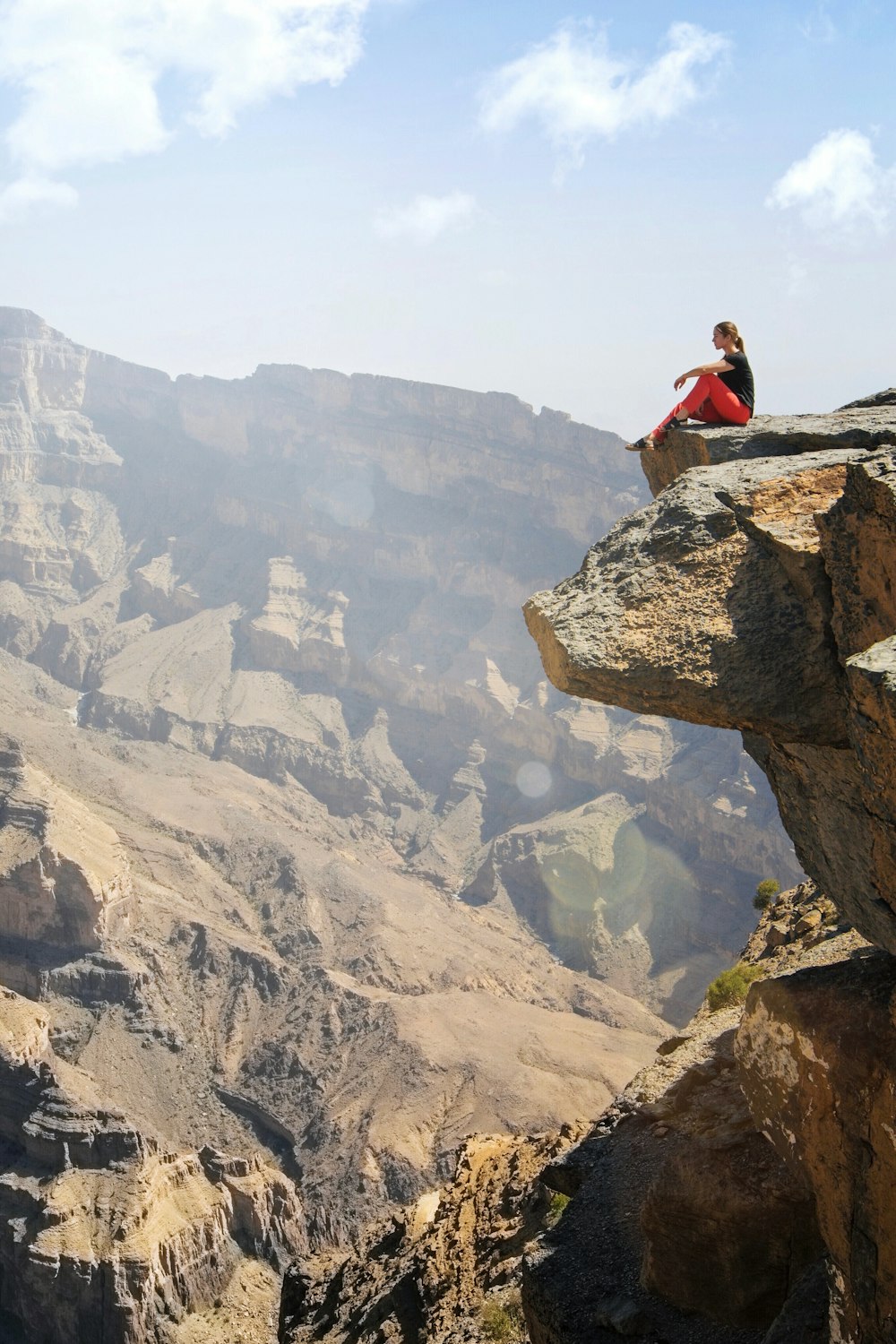 woman in red shirt sitting on rock formation during daytime