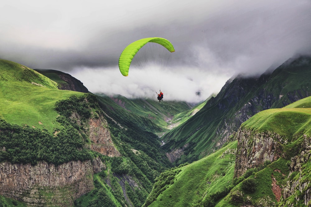 Persona in giacca rossa sulla montagna verde sotto il cielo grigio durante il giorno