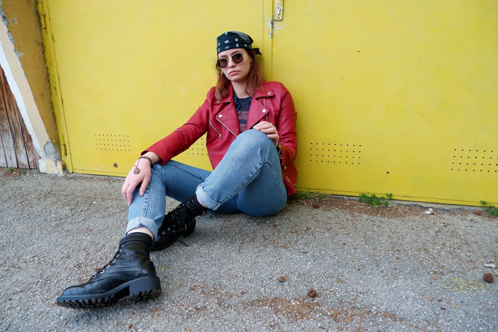 woman in blue denim jeans and pink jacket sitting beside yellow wall