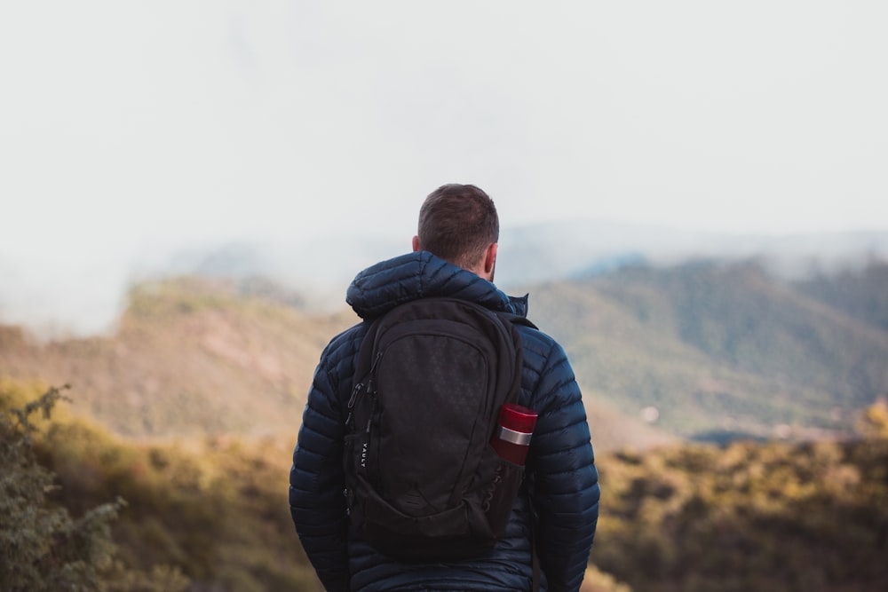 man in black jacket and black backpack standing on mountain during daytime