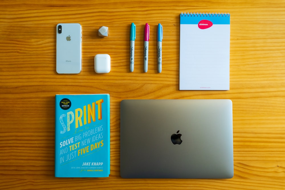macbook prateado ao lado de caderno branco e canetas