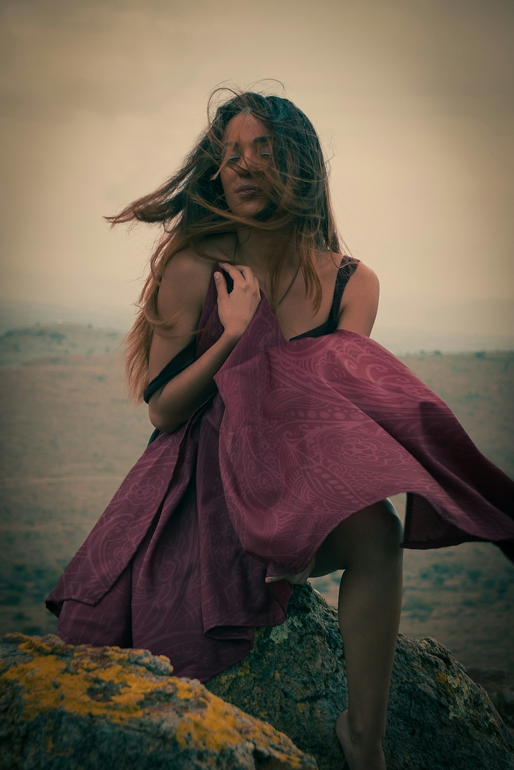 a woman in a purple dress sitting on a rock